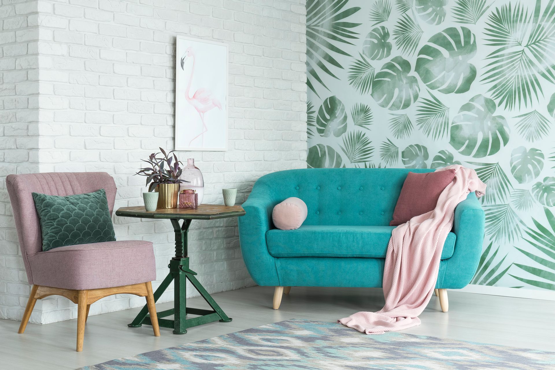 Living room with teal couch, pink chair, round table, and green leaf wallpaper.