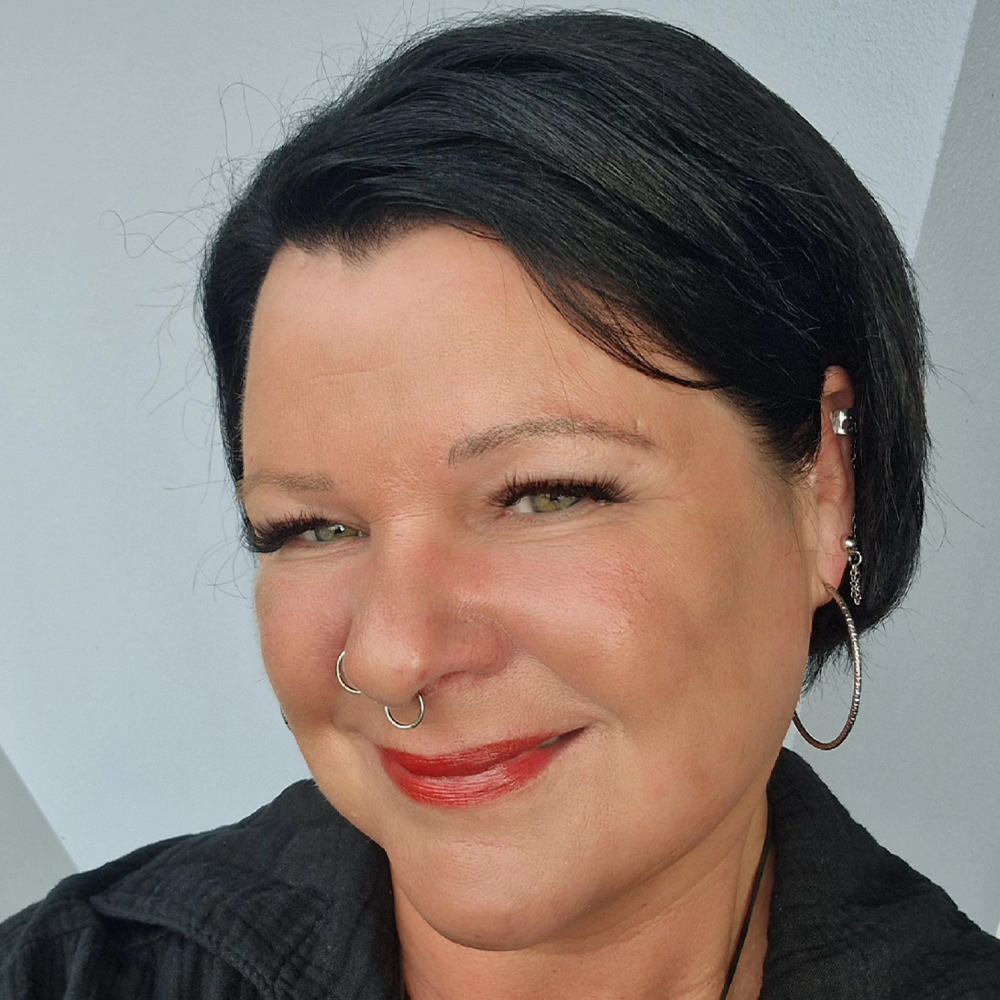 Eine Frau mit Nasenring und Creolen lächelt in die Kamera