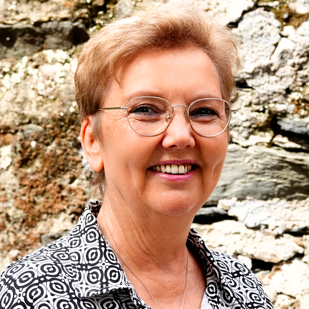 Eine Frau mit Brille und gemustertem Hemd lächelt vor einer Felswand.