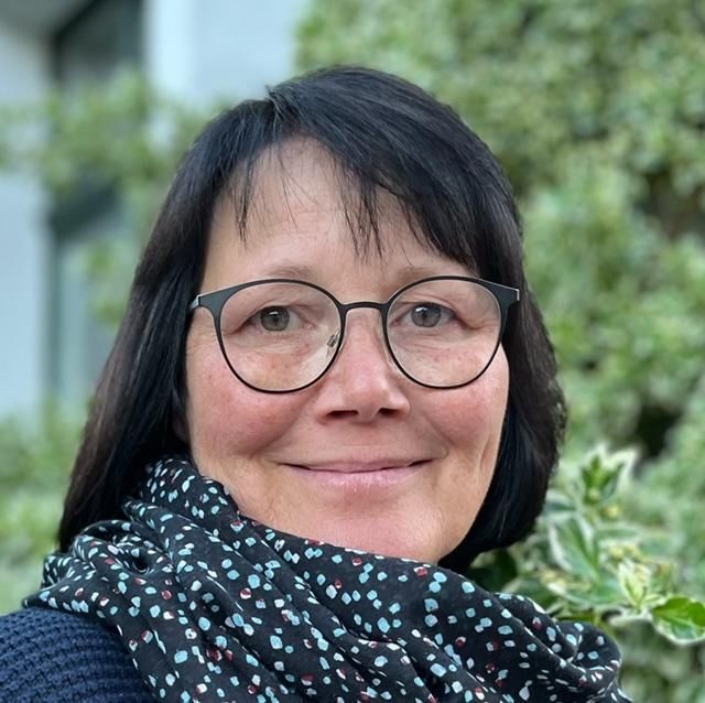 Eine Frau mit Brille und Kopftuch lächelt in die Kamera.