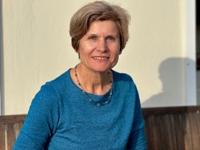 Eine Frau sitzt auf einer Bank und trägt einen blauen Pullover und eine Halskette.