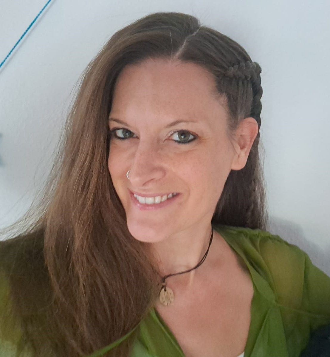 Eine Frau mit langen braunen Haaren lächelt und trägt ein grünes Hemd.