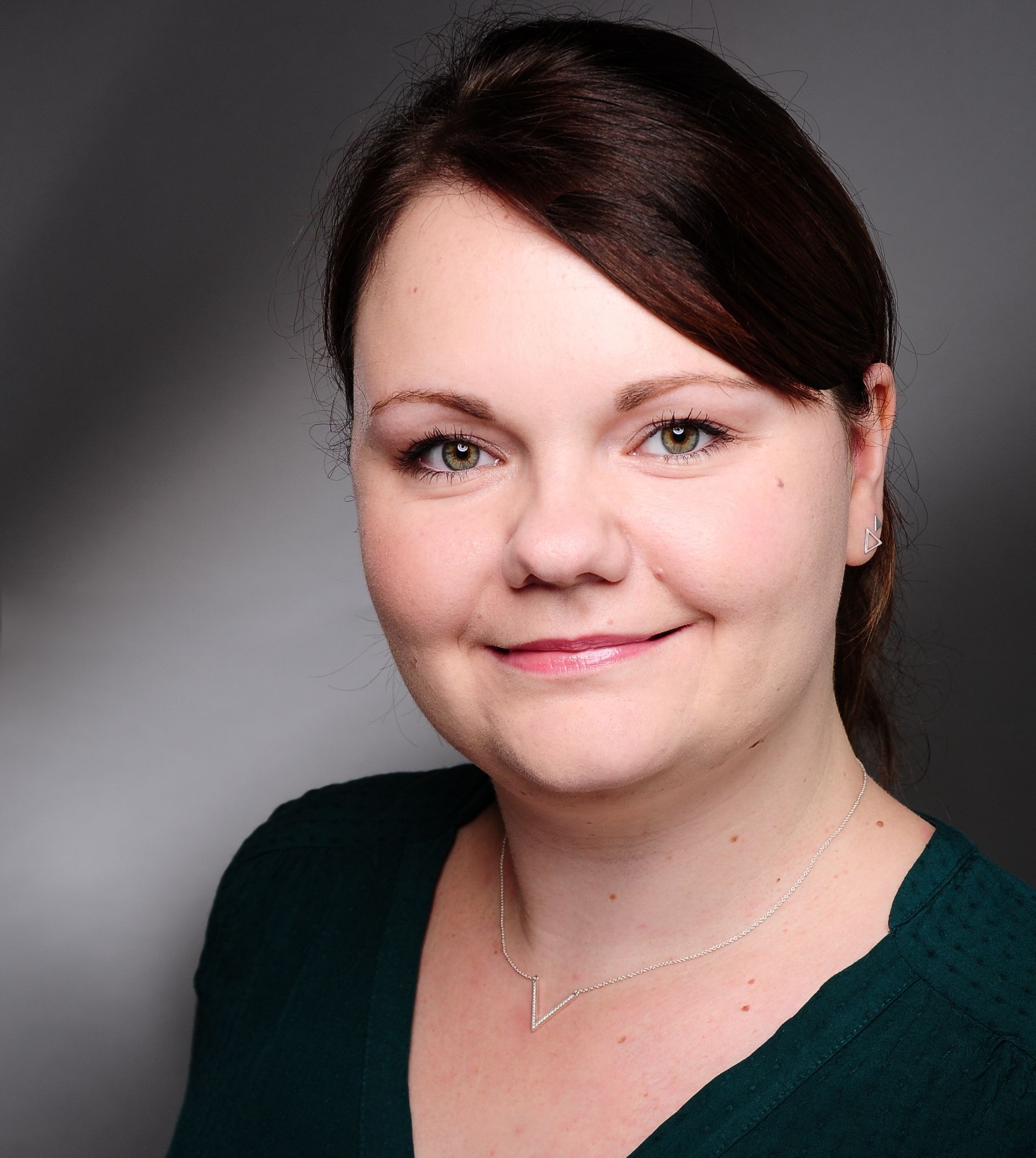Eine Frau mit einem grünen Pullover und einer Halskette lächelt in die Kamera.