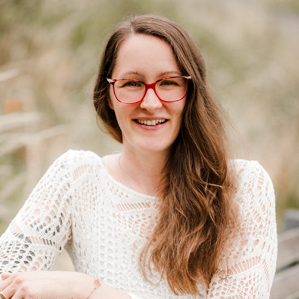 Eine Frau mit Brille und weißem Hemd lächelt in die Kamera.