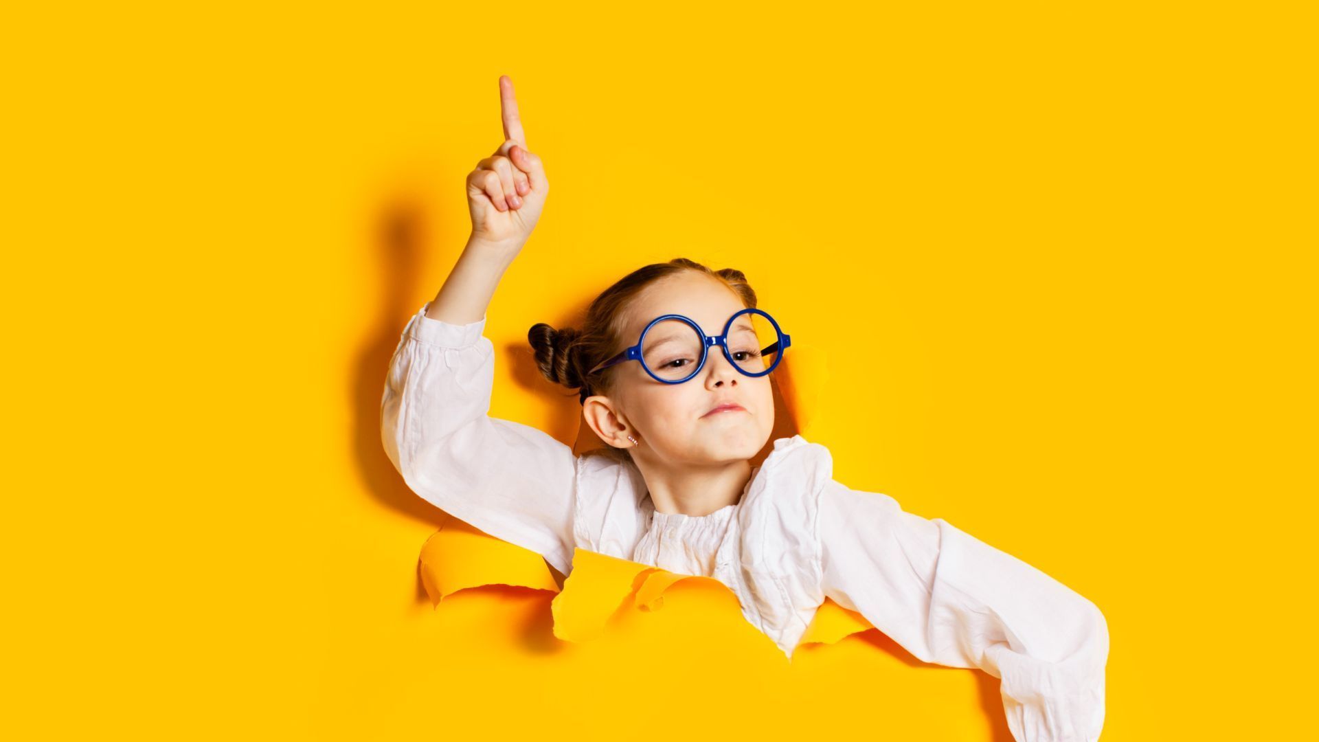 Mädchen mit Brille zeigt nach oben, taucht vor gelbem Hintergrund auf und referiert zu einem Thema.