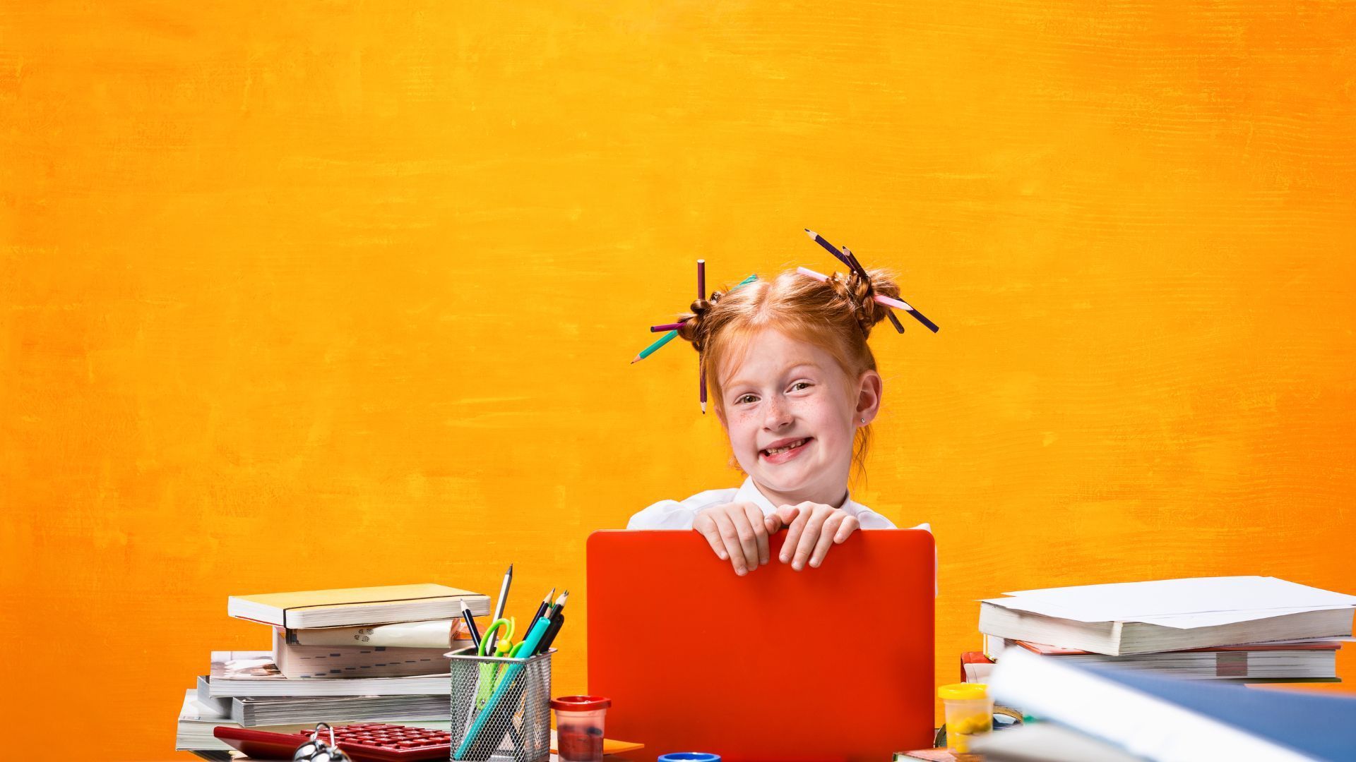 Ein kleines Mädchen sitzt mit einem Laptop und Büchern an einem Schreibtisch.