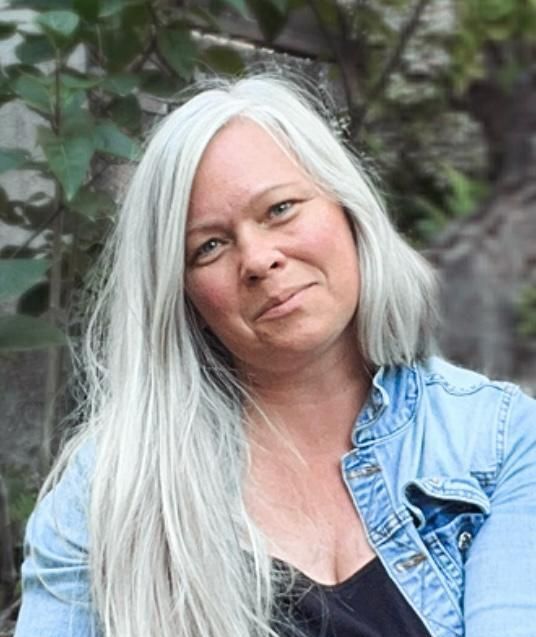 Eine Frau mit langen grauen Haaren trägt eine blaue Jeansjacke.