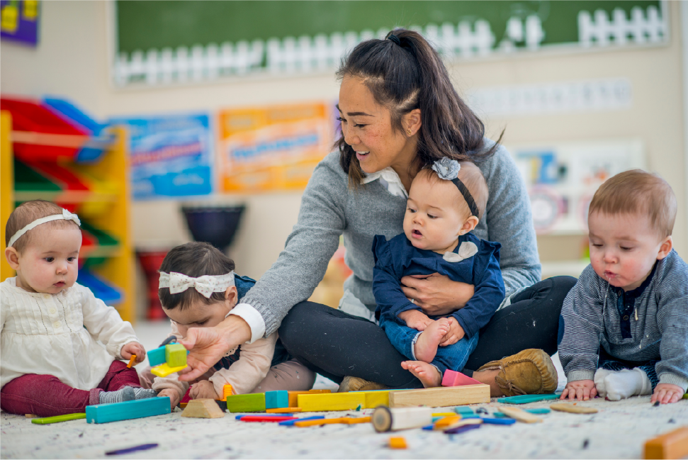 Eine Frau sitzt auf dem Boden und spielt mit drei Babys.