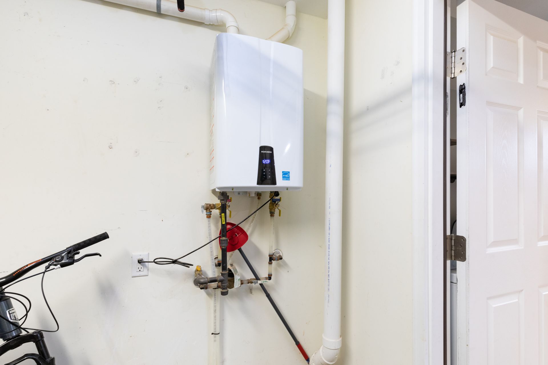 Wall-mounted tankless water heater with connected pipes and valves inside a utility room. Wall-mounted tankless water heater with connected pipes and valves inside a utility room.