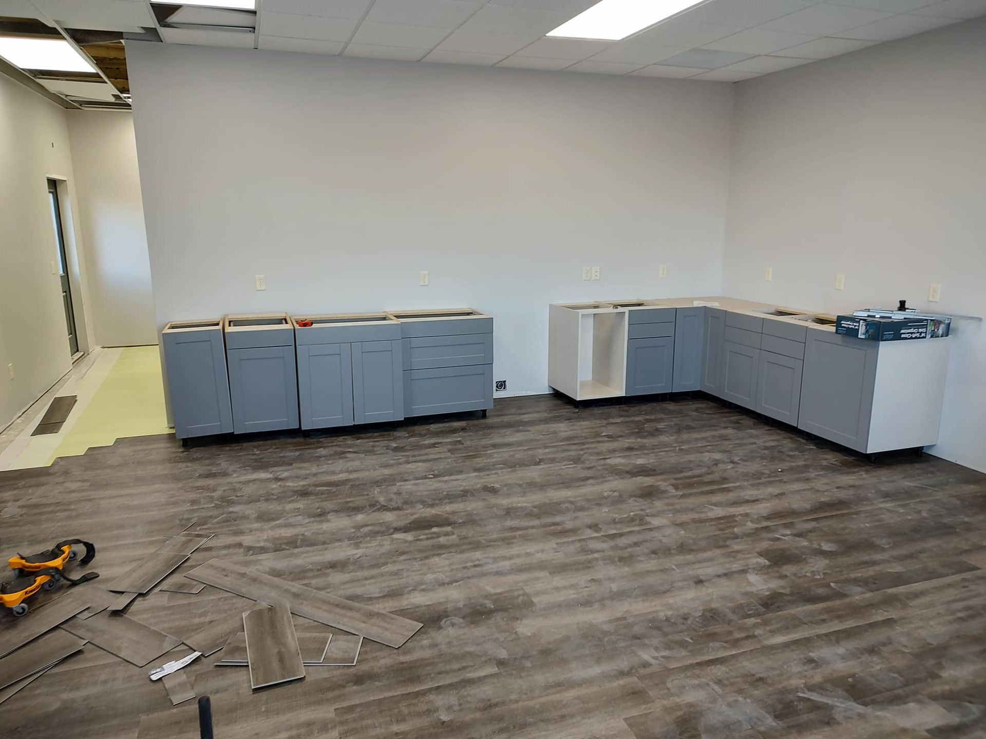 Cabinets being installed in a room with gray walls and wood-look flooring. Tools lie on floor.