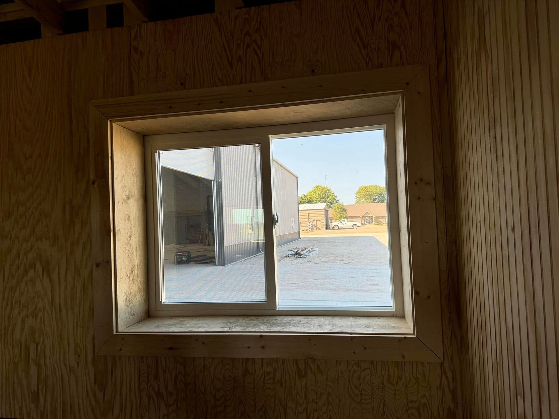 Window in unfinished wooden structure looking out to a bright outdoor area.