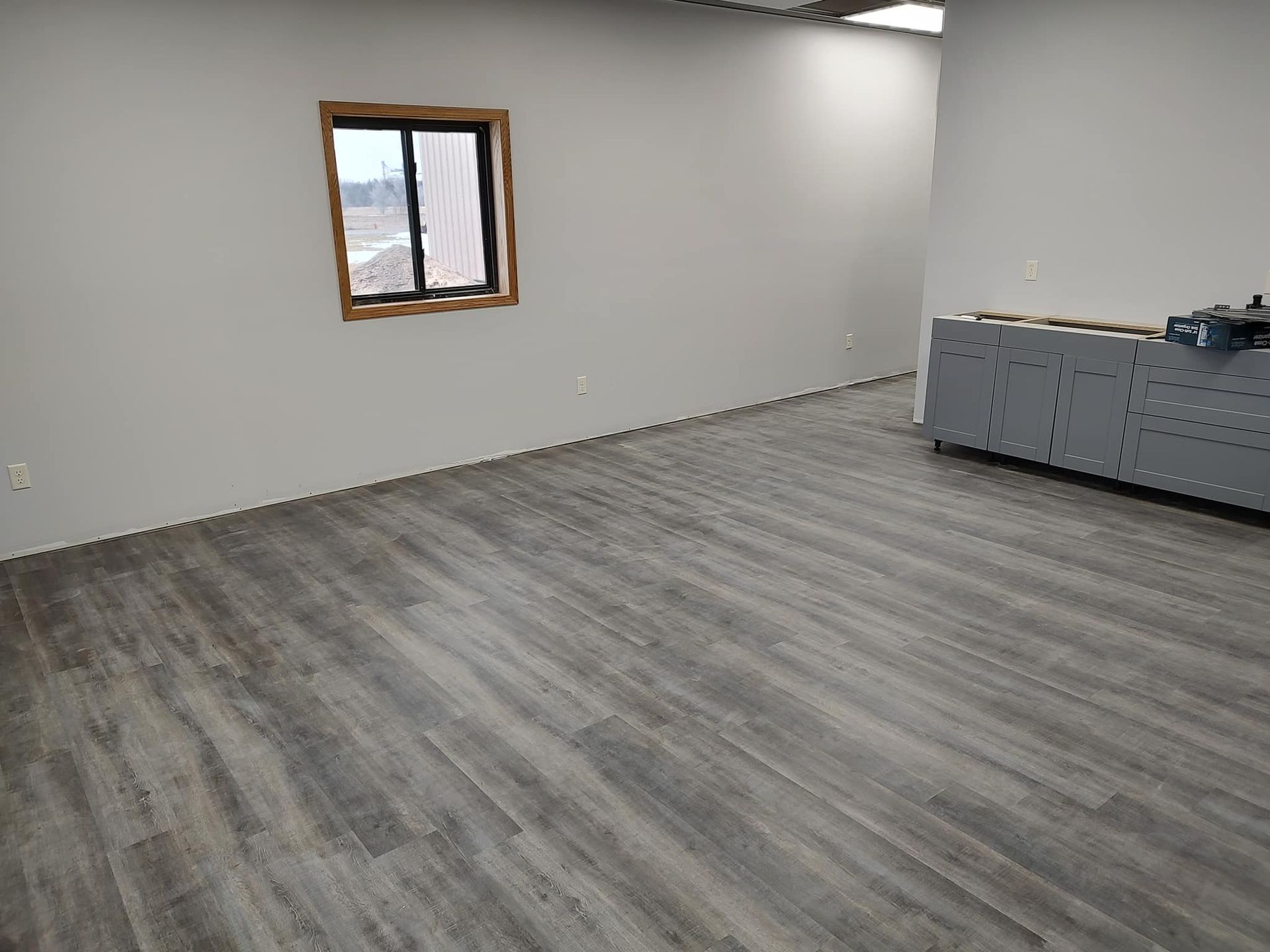 Empty room with wood-look flooring and gray walls. Window on the left, gray storage unit on the right.