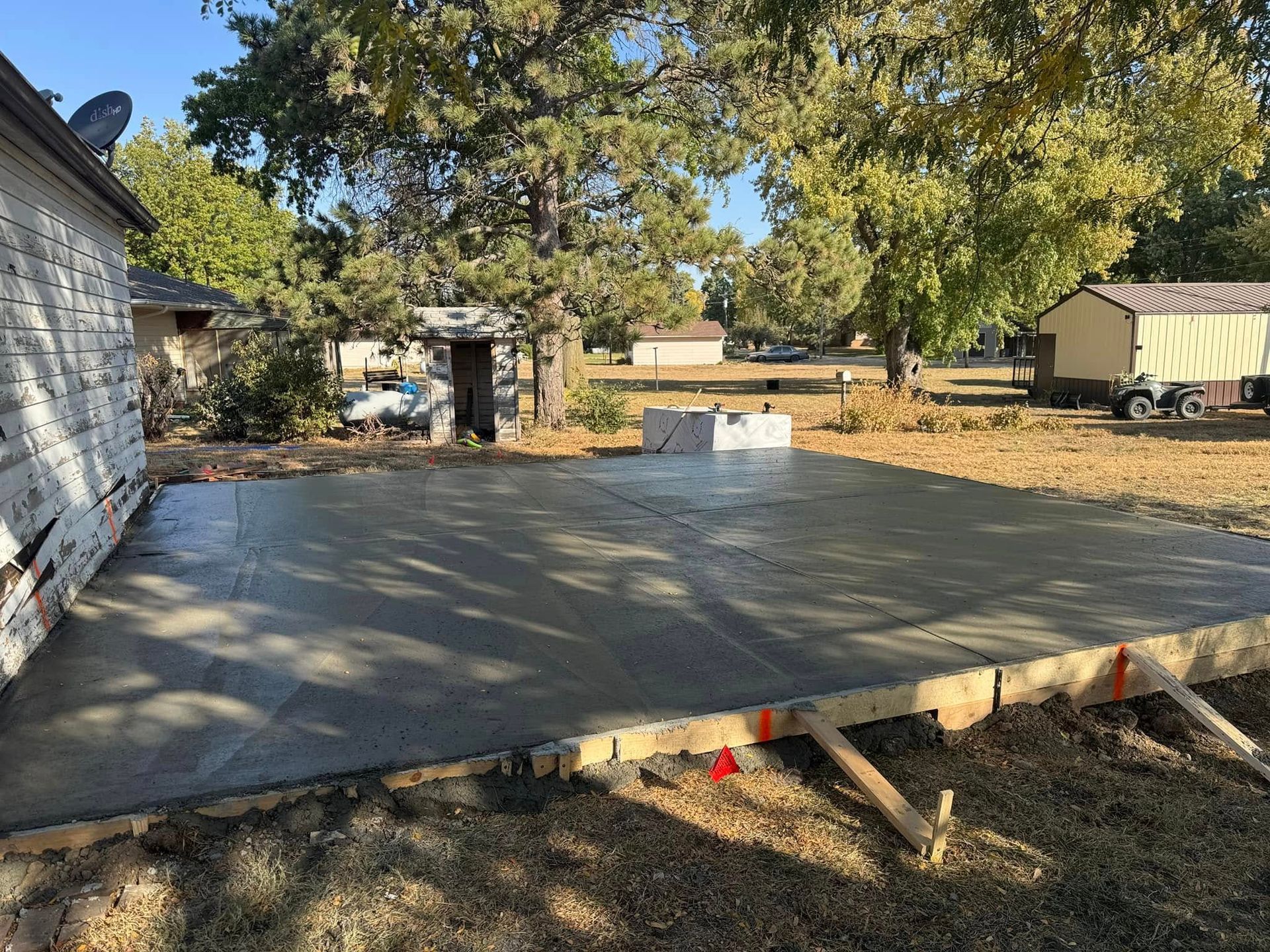 Freshly poured concrete patio in a backyard setting. Wooden forms visible.