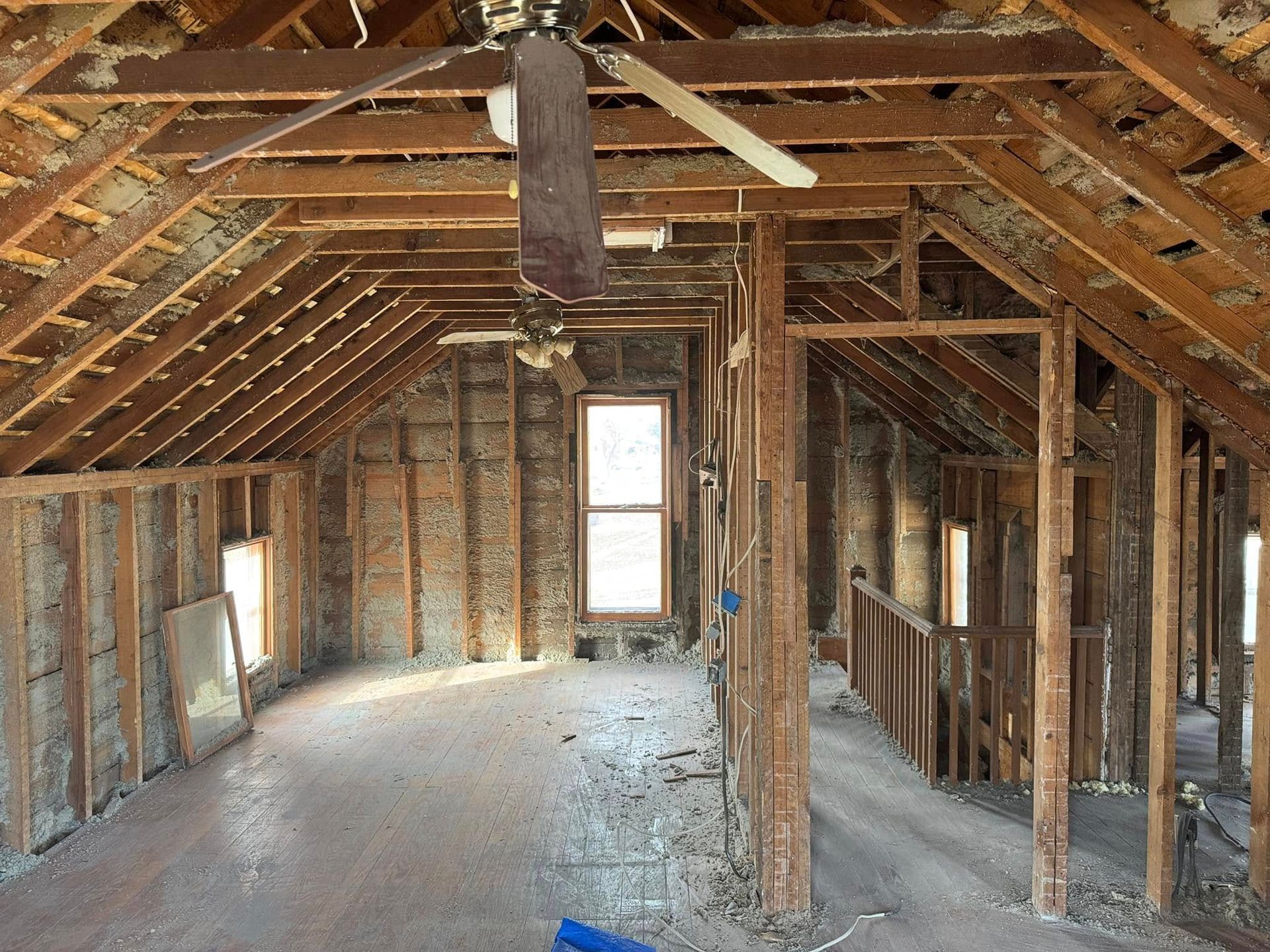 Interior view of a partially renovated attic space with exposed wooden beams, studs, and a window.
