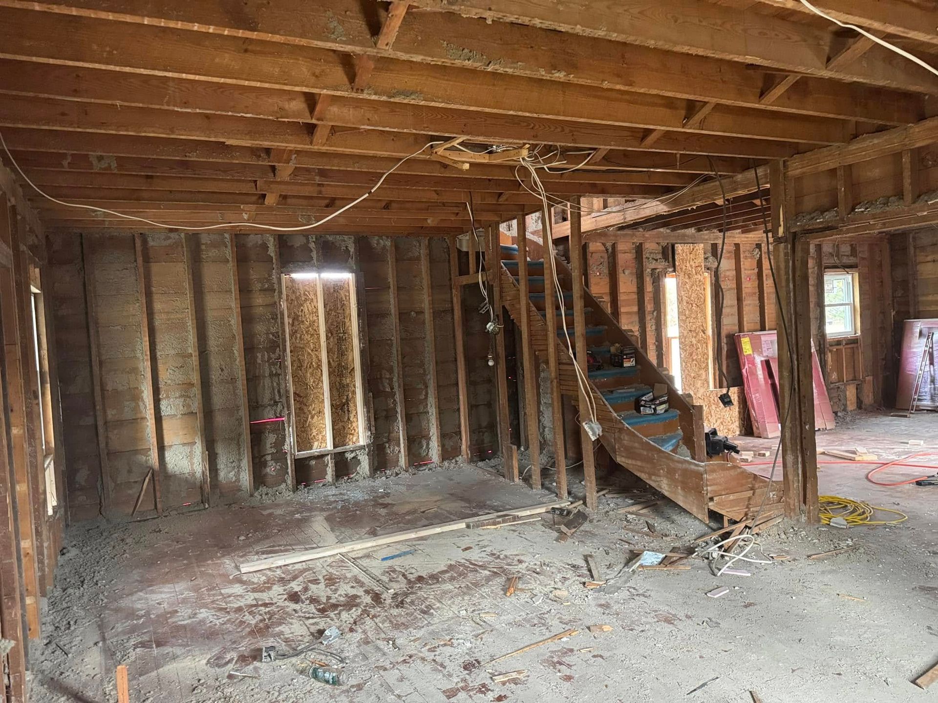 Interior of a house under renovation; exposed wooden studs, stairs, and debris on the floor.