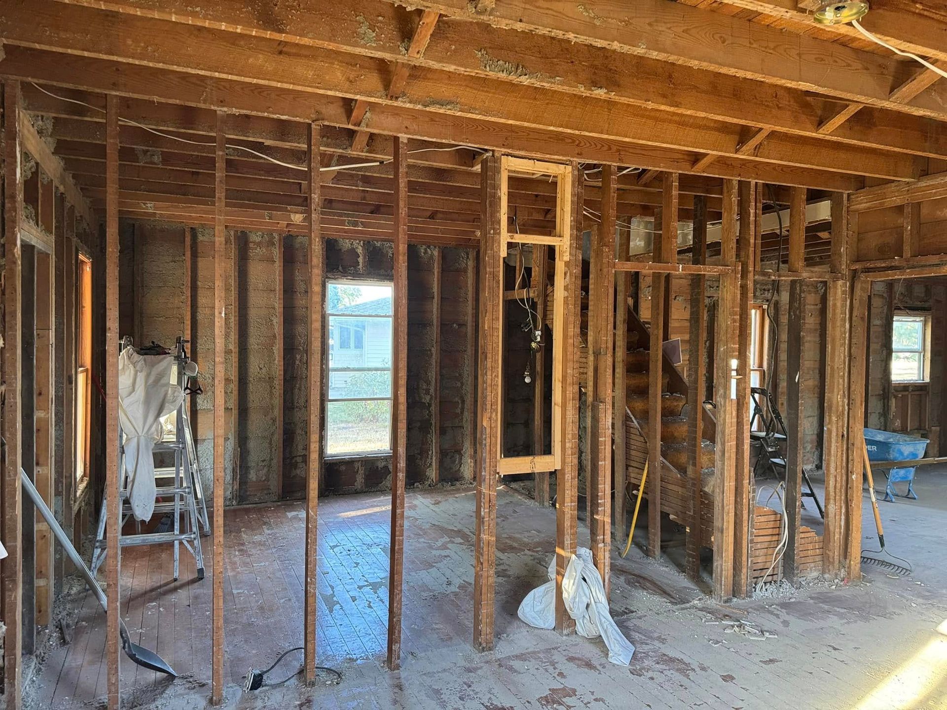 Interior house framing stripped of walls, showing studs, window, and debris.