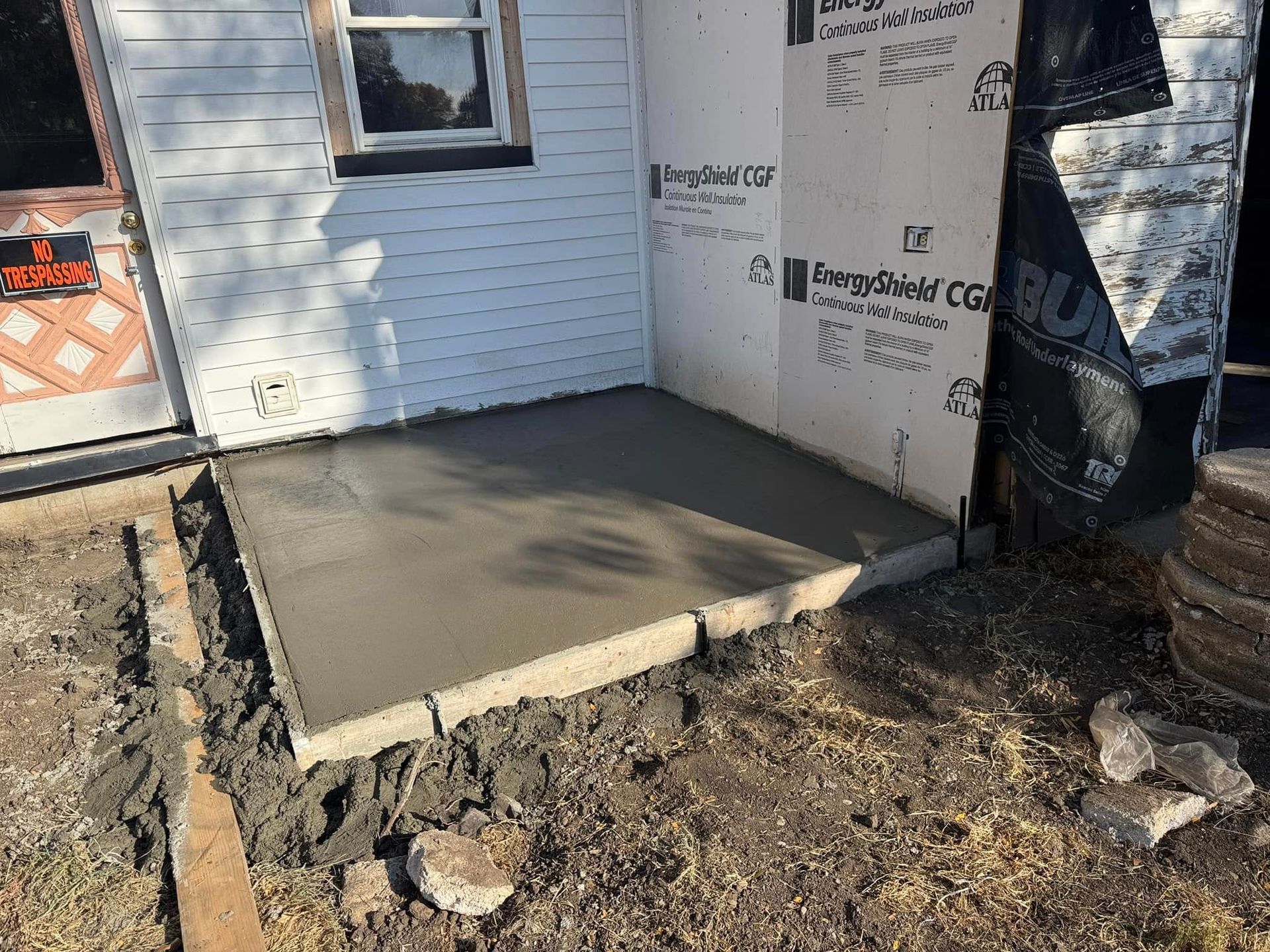 Newly poured concrete porch with brick border next to a house with exposed siding.