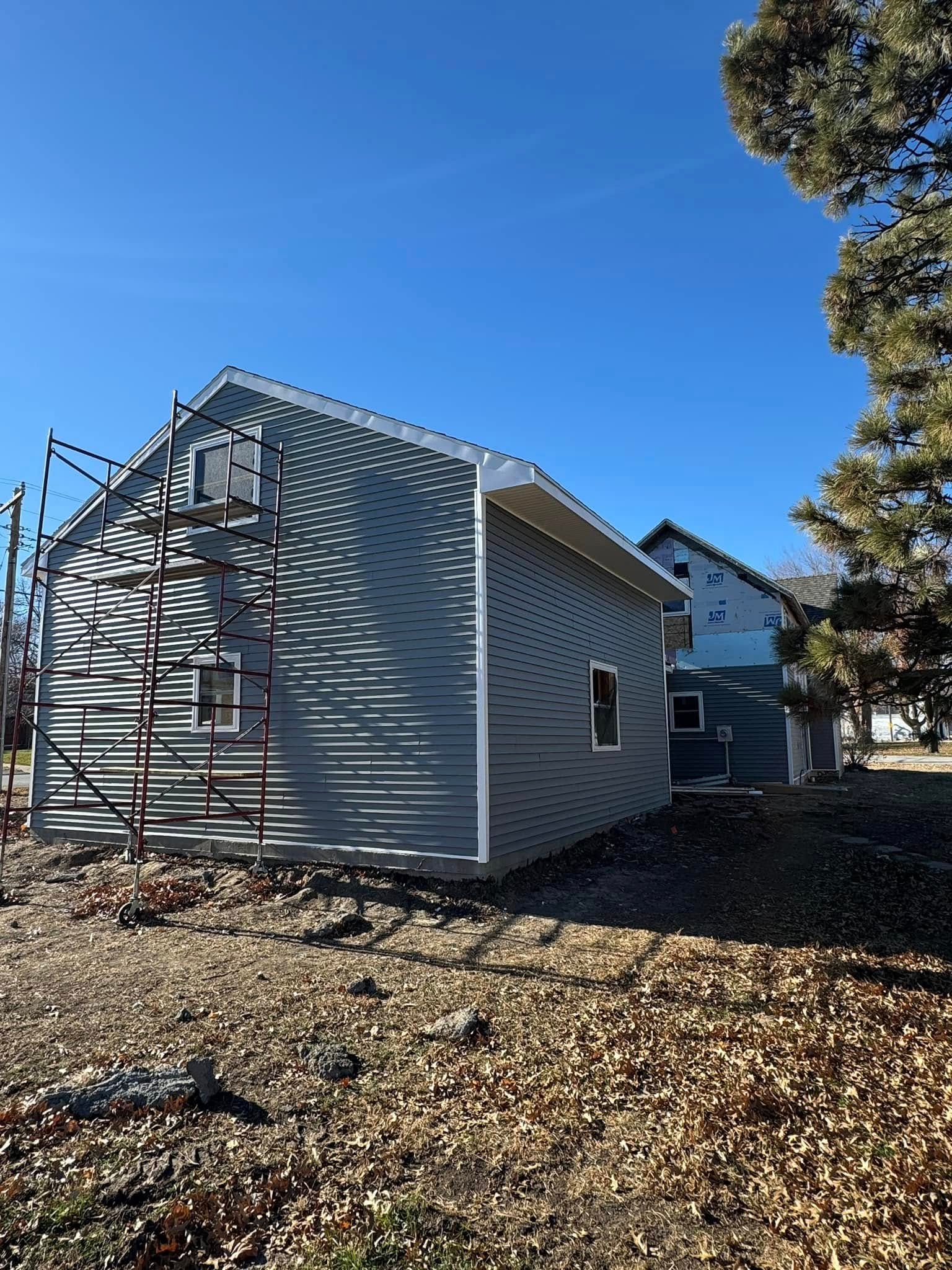 Side view of a light blue building with scaffolding, another building in the background, blue sky, and dry brush.