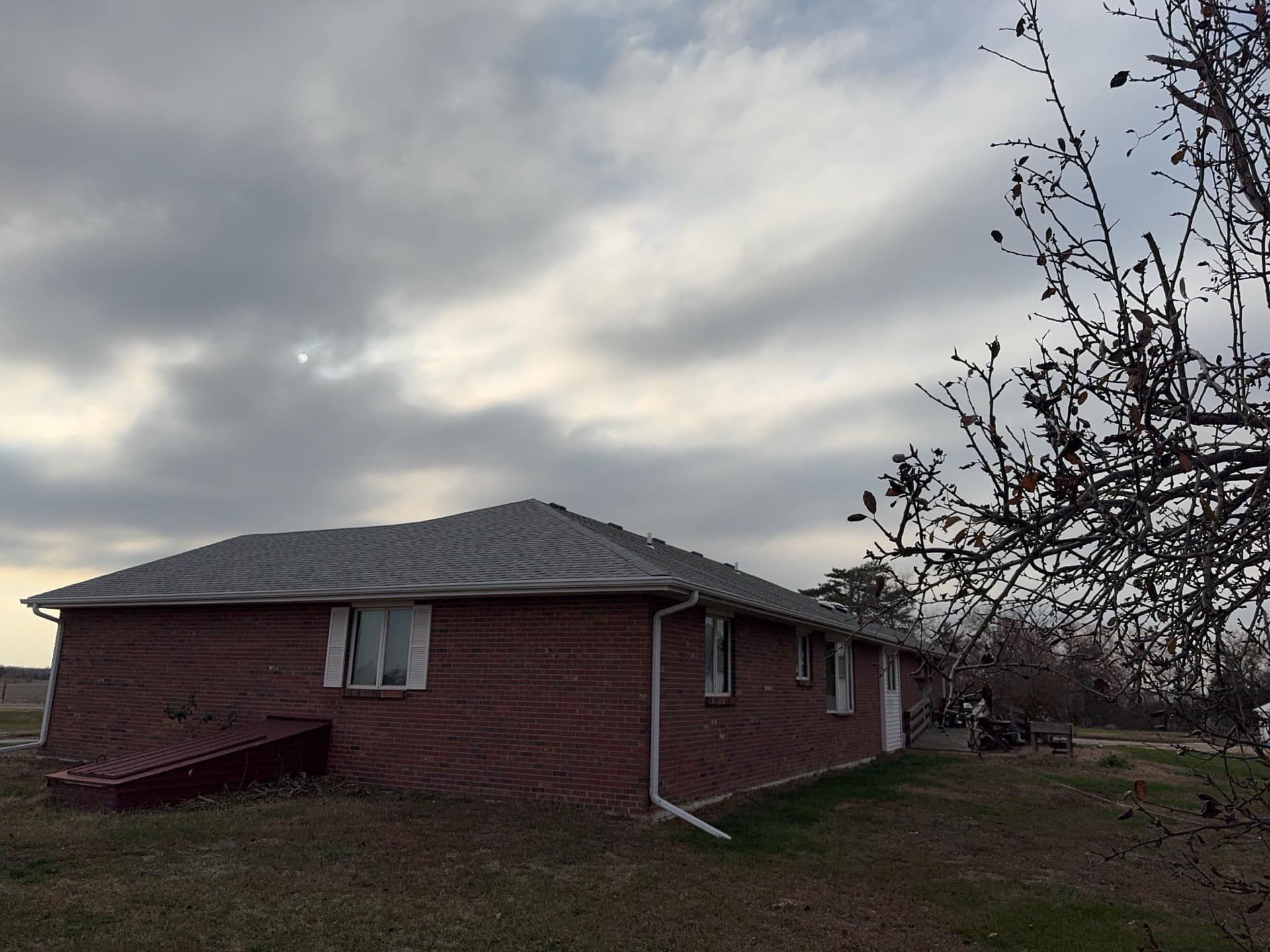Red brick house under a cloudy sky, with a leafless tree in the foreground.