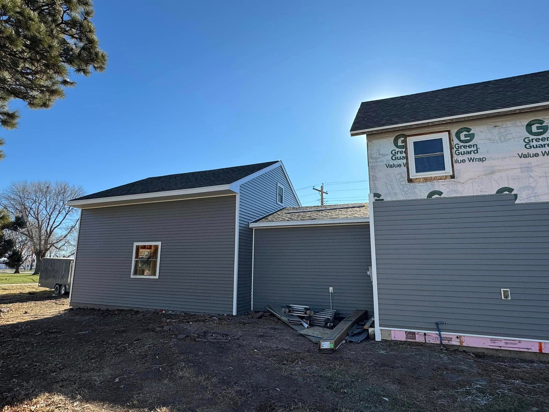 Exterior of a house under construction; gray siding with a black roof and blue sky.
