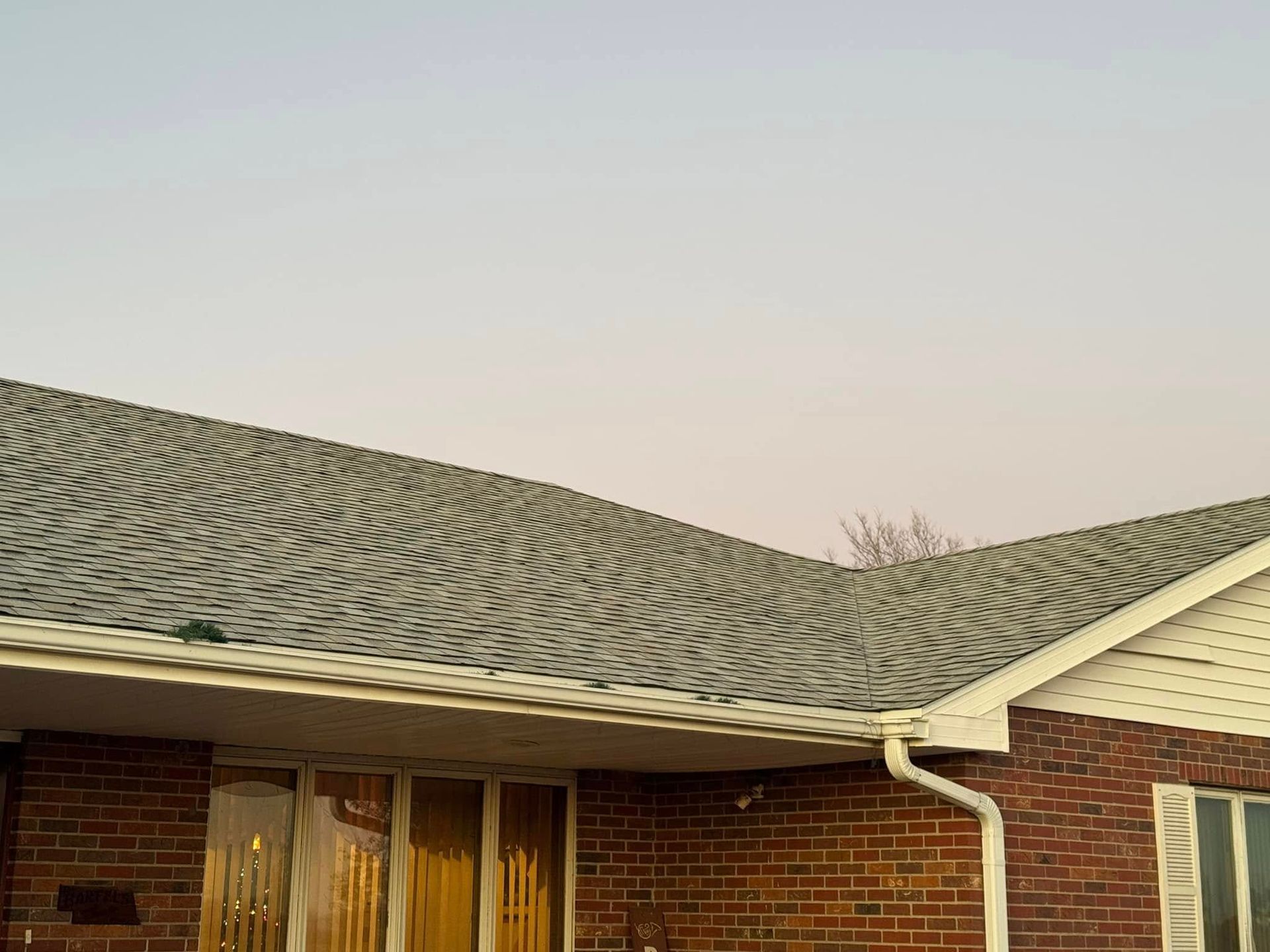 Brick house with gray wavy roof, white gutters, and light purple sky.