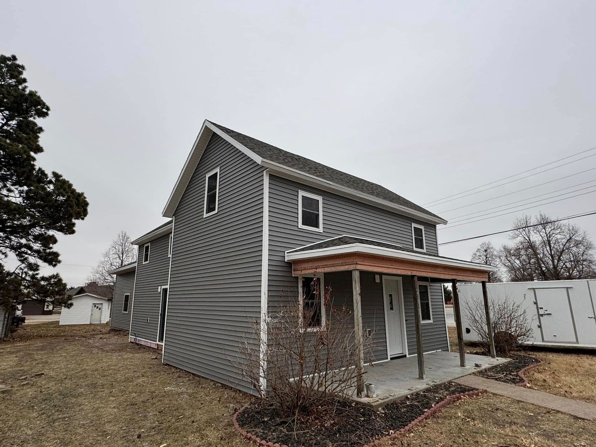 Two-story gray house with porch under a cloudy sky.