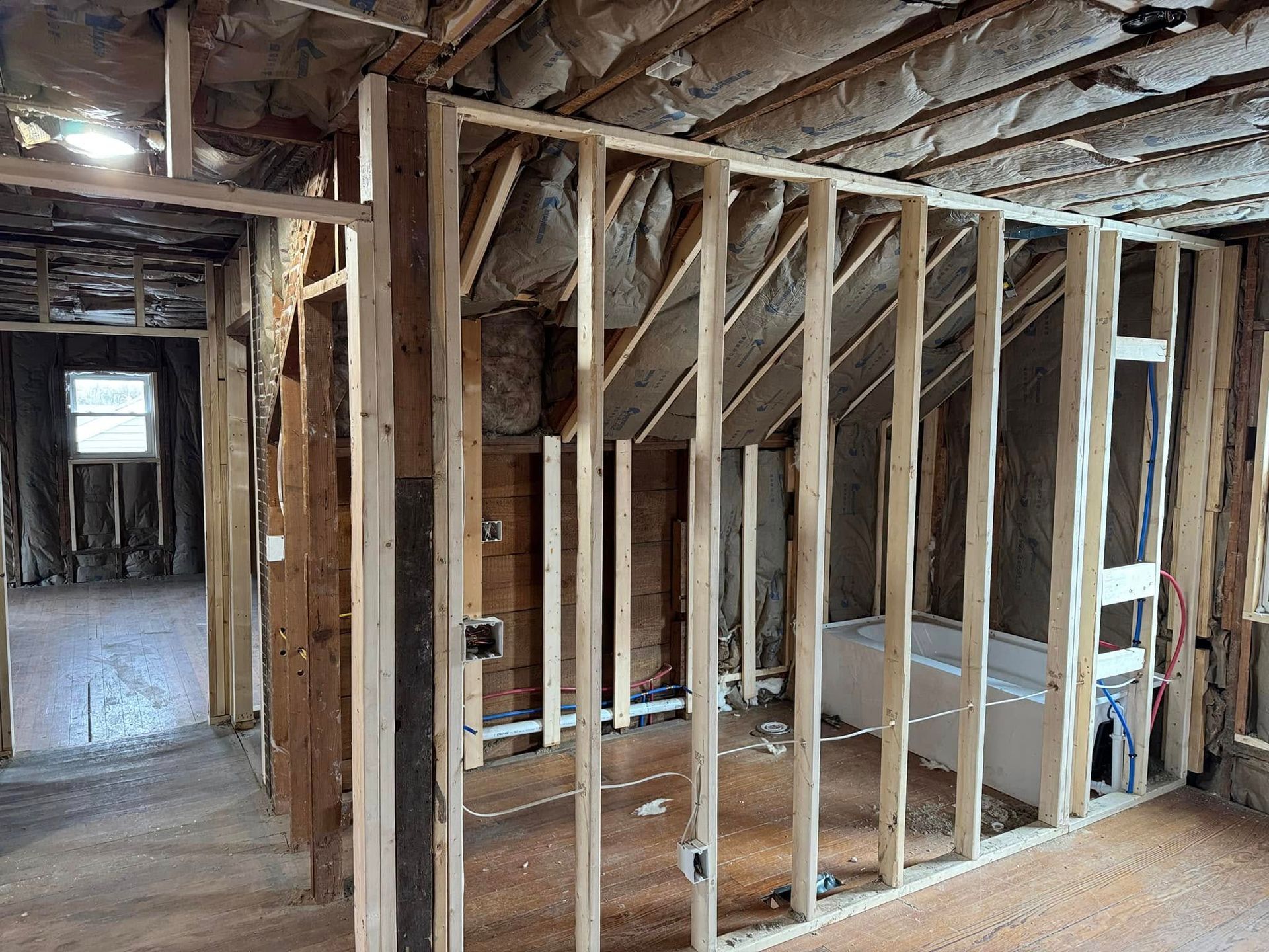 Interior view of a building under construction, showing wooden framing, insulation, and a partially built wall.