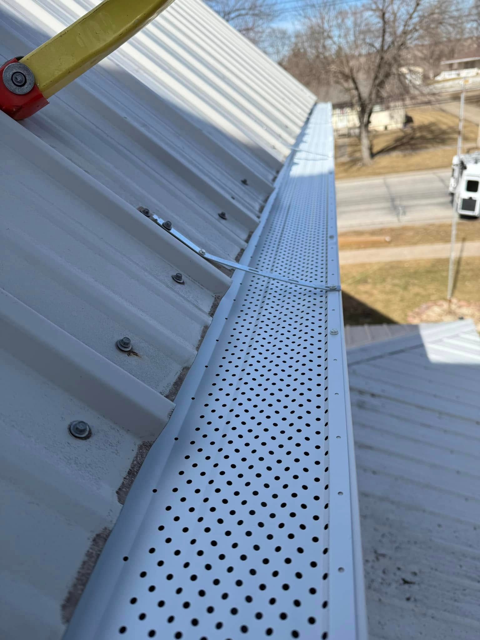 A gutter with numerous small holes runs along a metal roof edge.