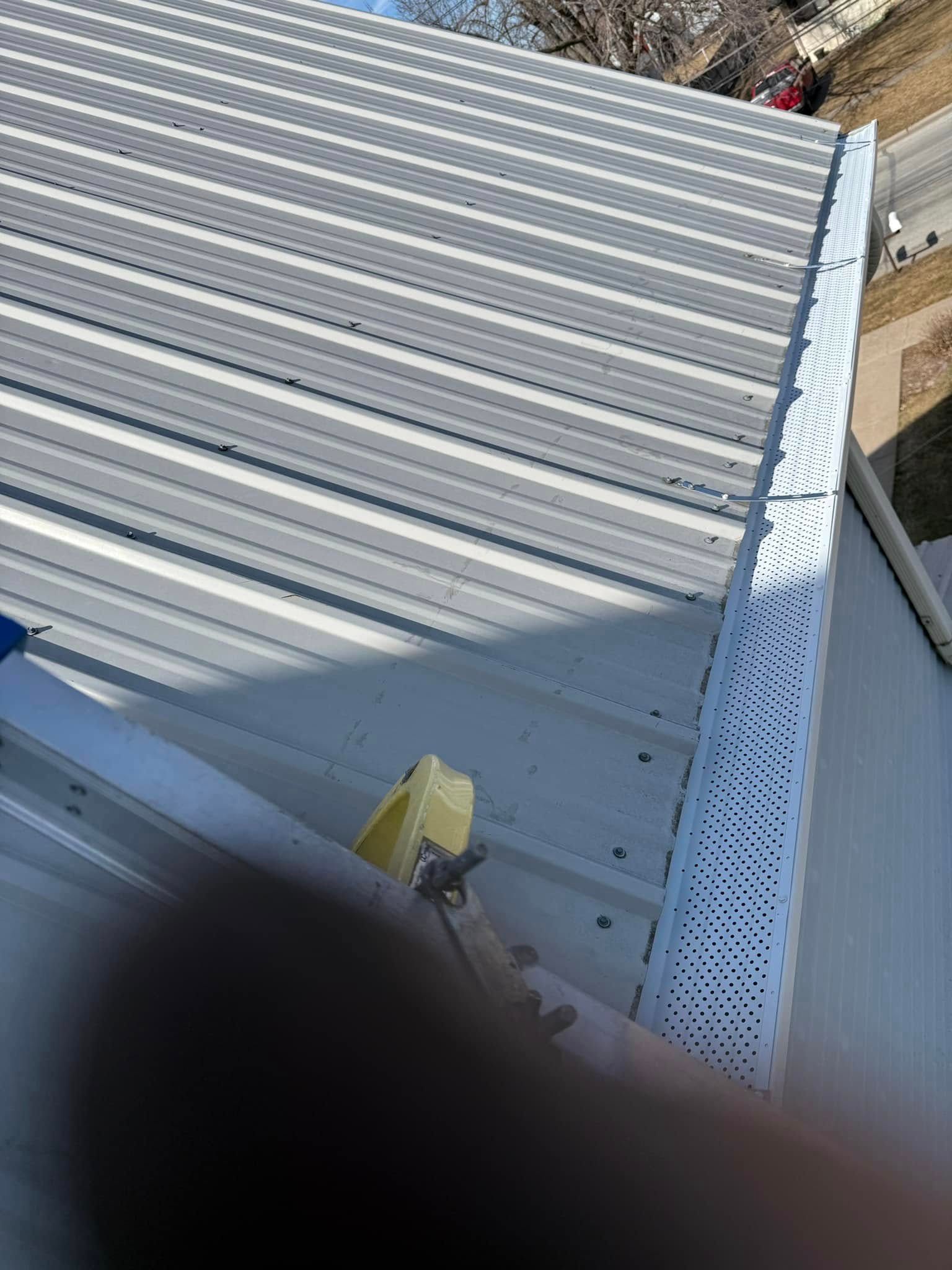 Metal roof with white gutter, ladder, and yellow tool.