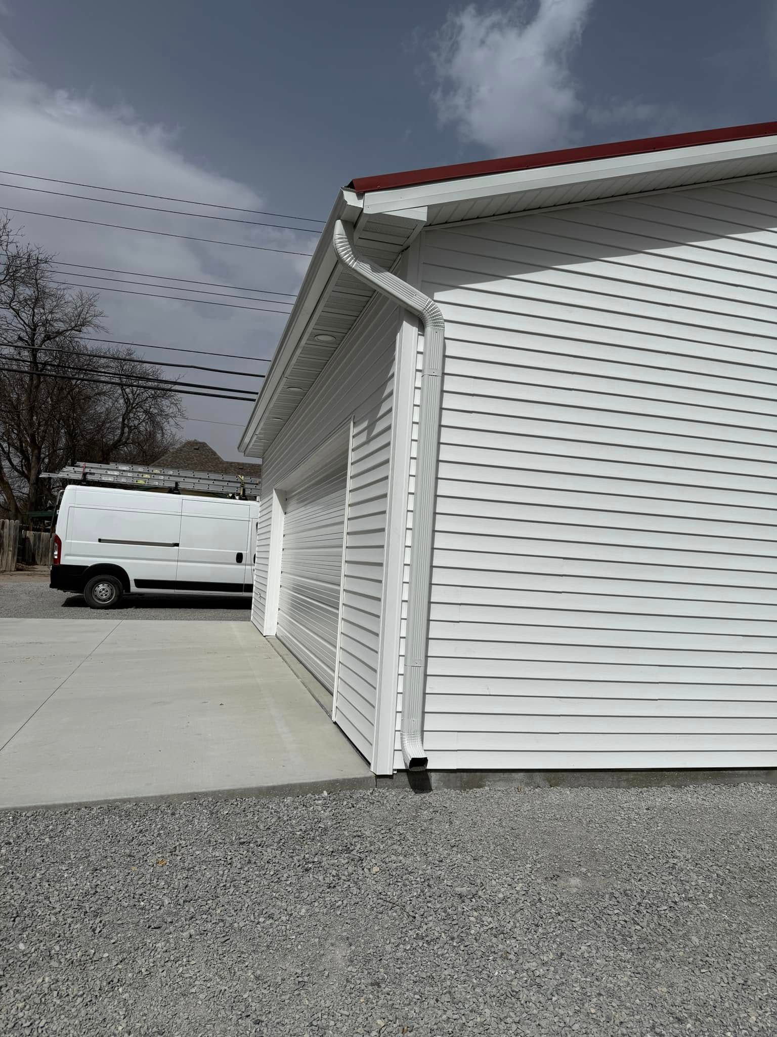White building with corrugated siding, gutter, red roof trim, parked white van, gravel ground.