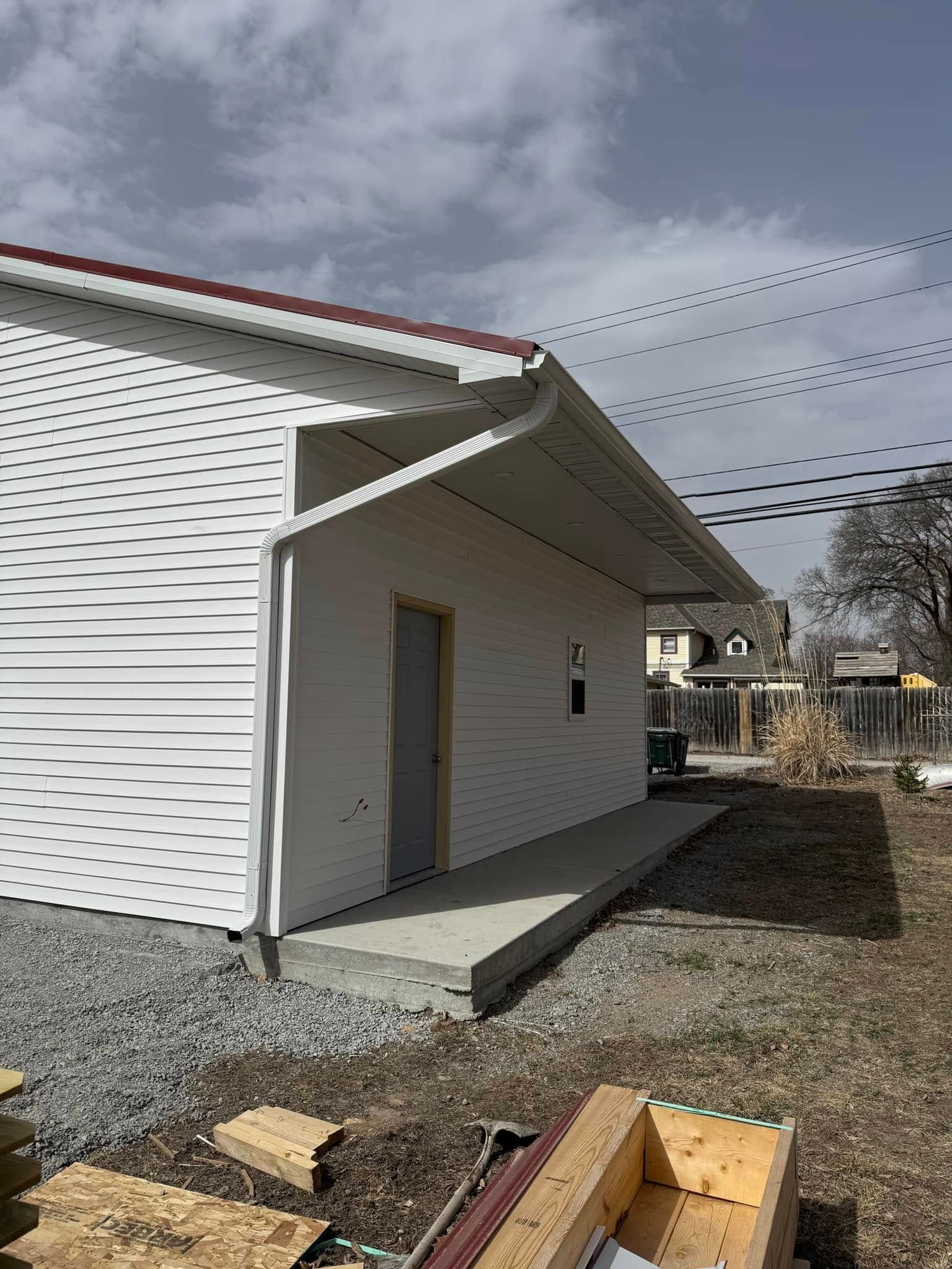 White building with red roof, gray door, and concrete porch under cloudy sky.