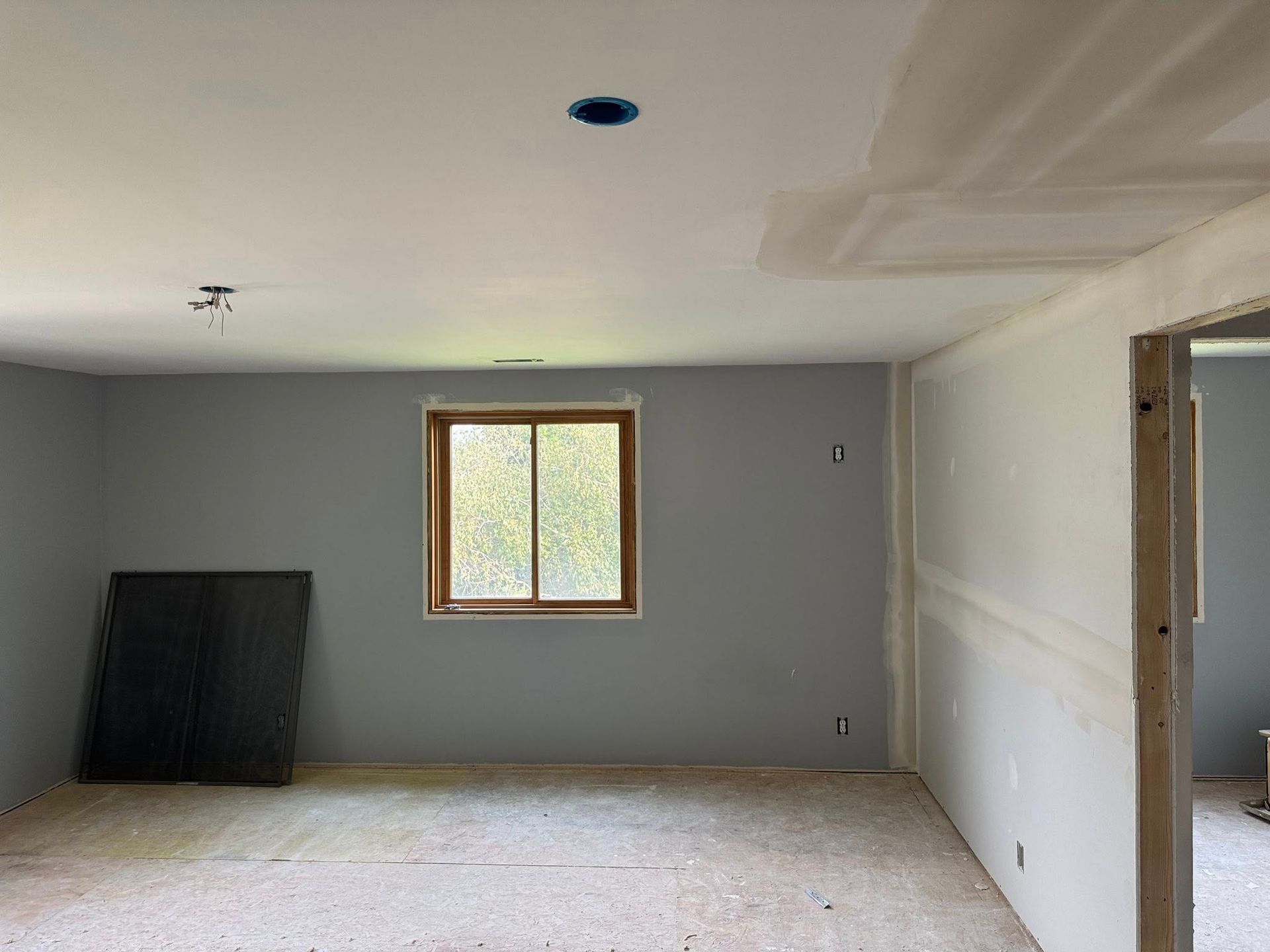 Room under construction with gray walls, window, exposed drywall, and unfinished floor.