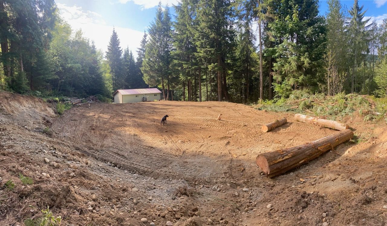 A dirt field with a house in the background and trees in the background.