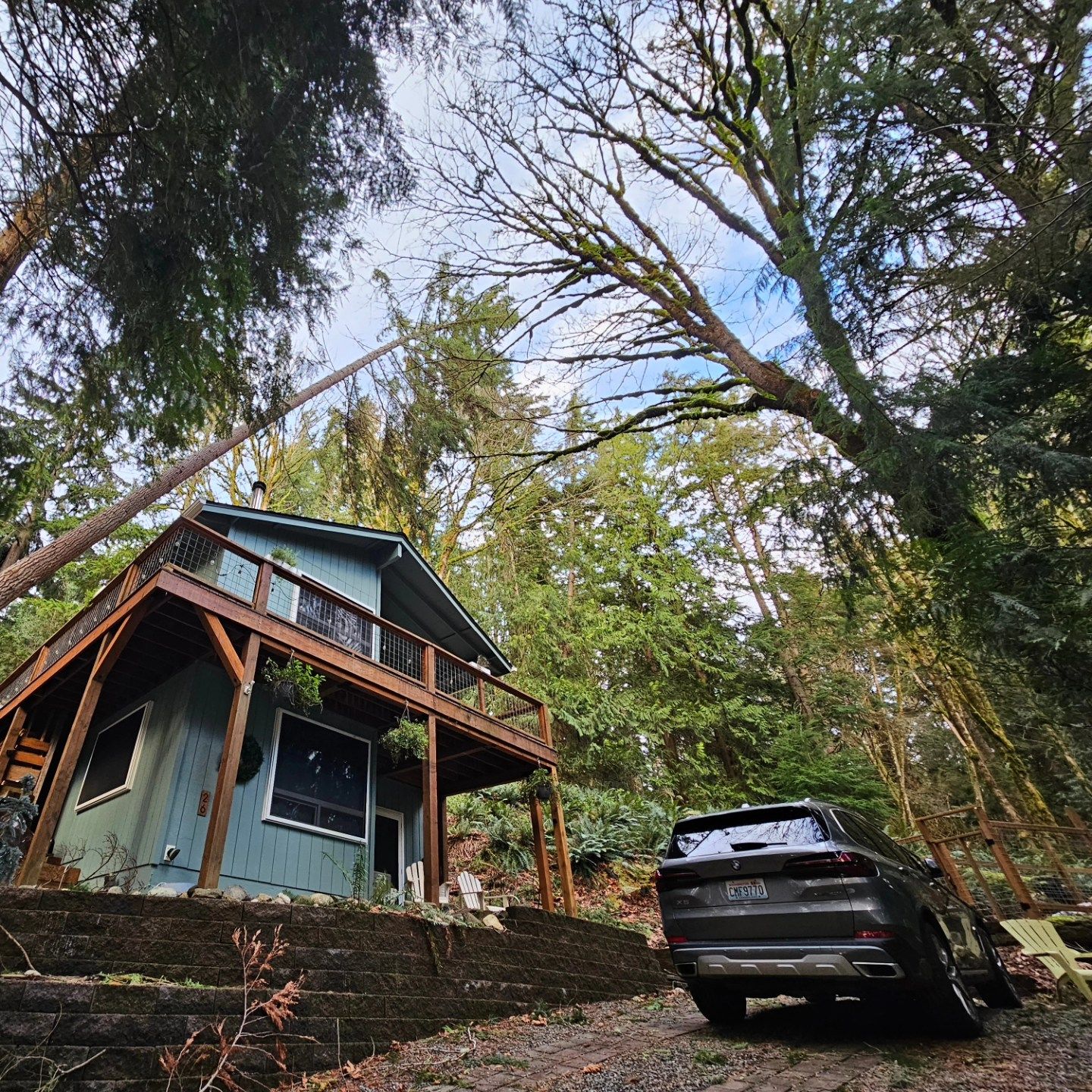 A car is parked in front of a house in the woods.