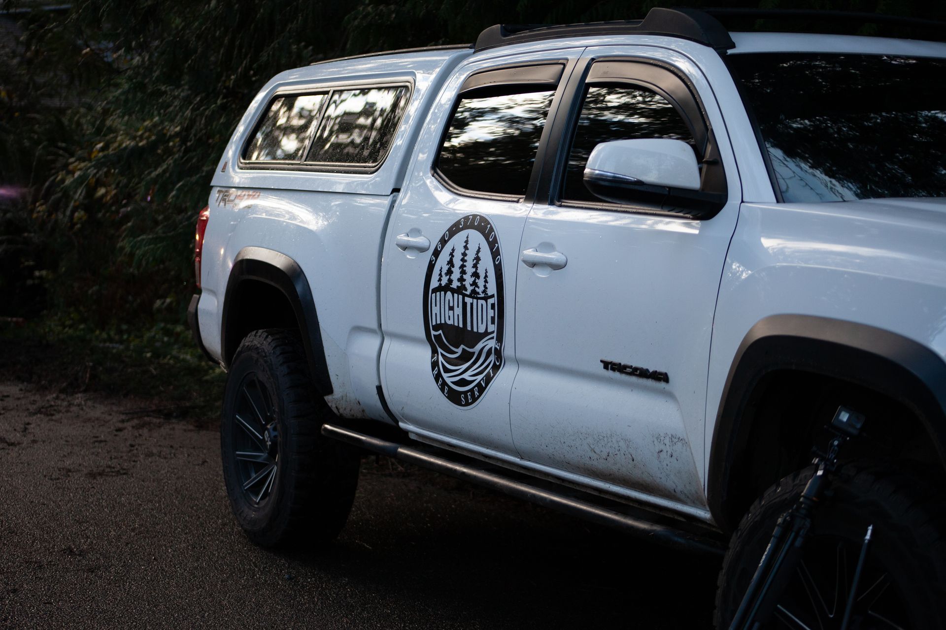 White Toyota Tacoma truck with black emblem, black wheels, and bed cap.