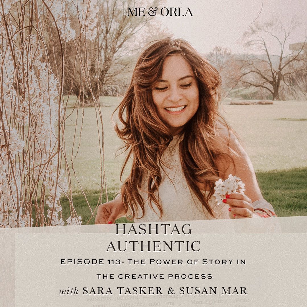 A woman is smiling while holding a flower in front of a tree.