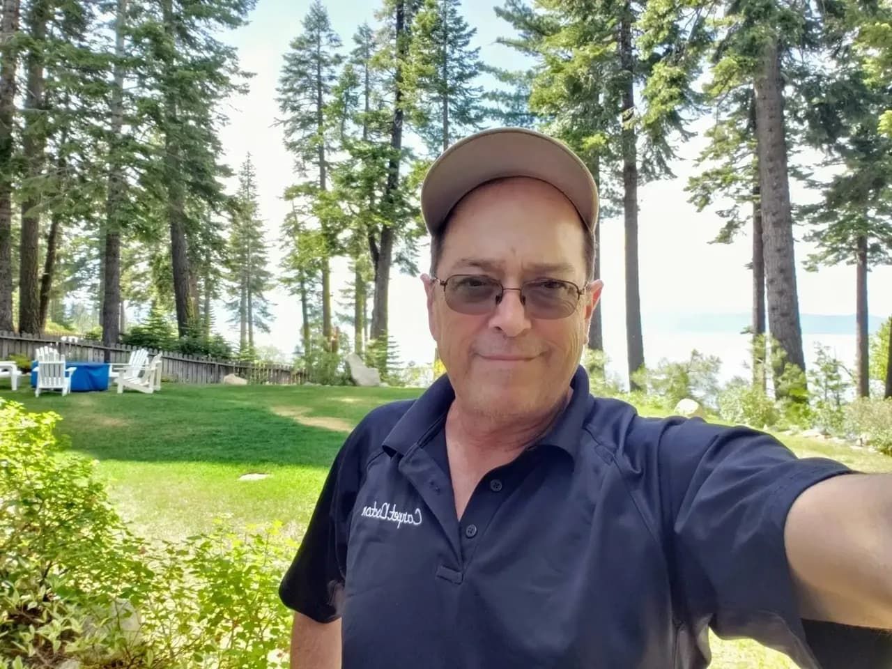 A man wearing a hat and glasses is taking a selfie in front of trees.