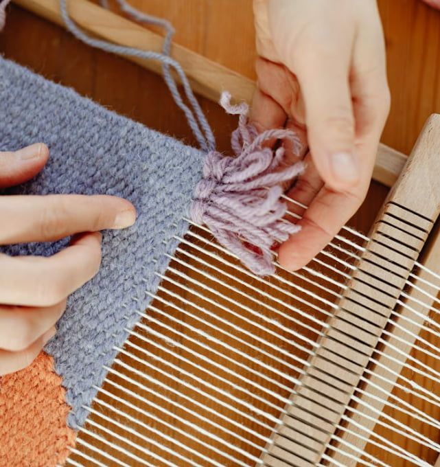 A person is weaving a piece of fabric on a loom