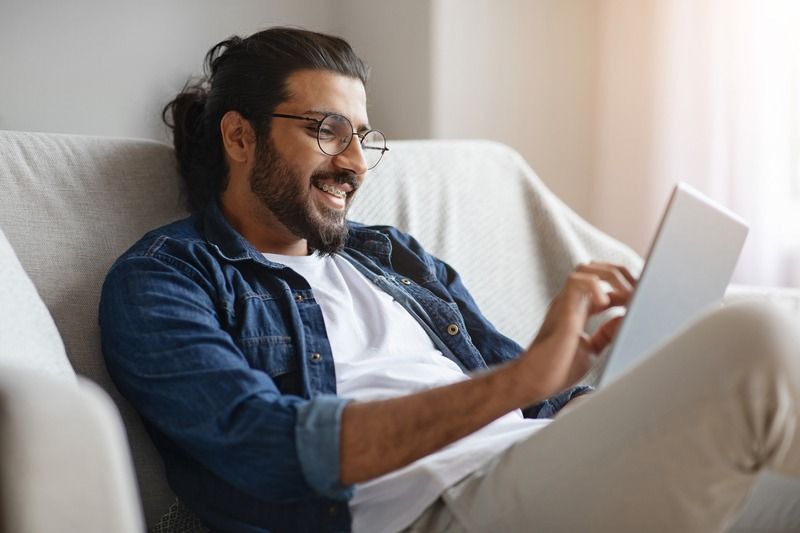 a man wearing glasses is sitting on a couch using a tablet