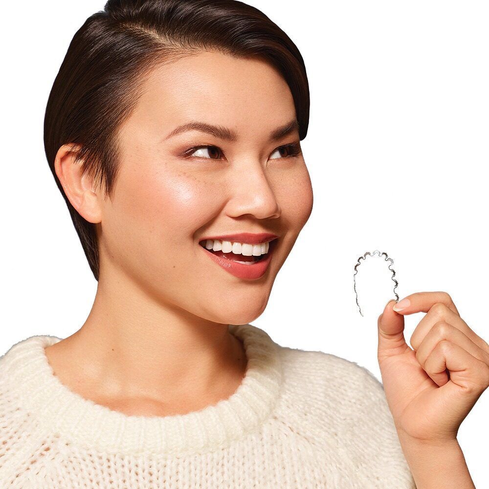 a woman in a white sweater is holding a clear retainer in her hand