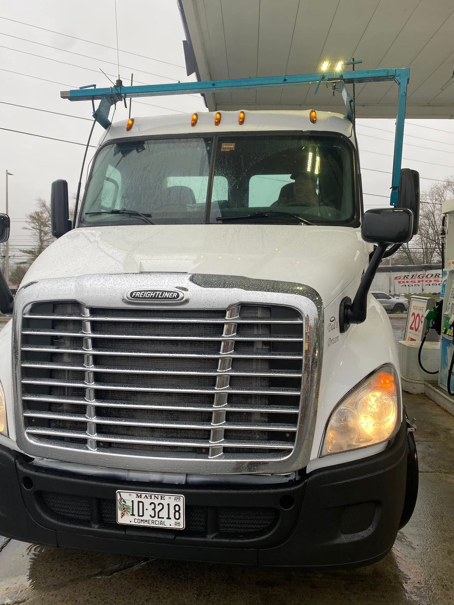 White Freightliner truck at a gas station with a blue bar on top.
