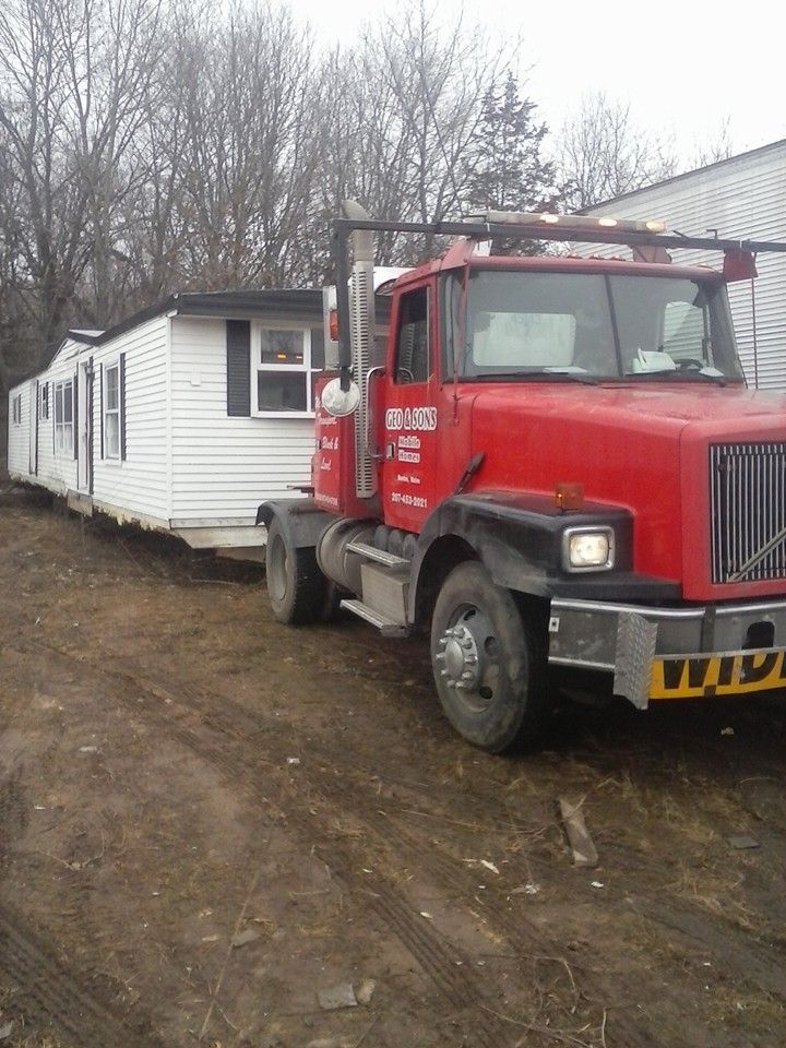 Red semi-truck towing a white mobile home on a dirt road.