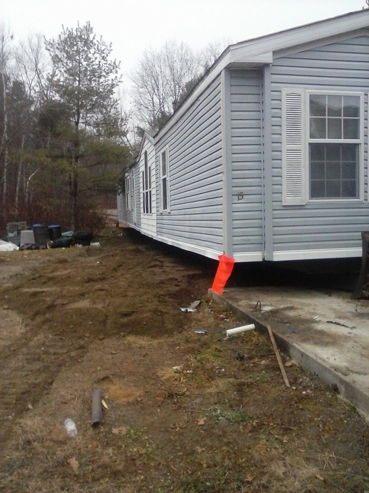 A light blue mobile home on dirt. Orange pipe and other materials sit nearby.