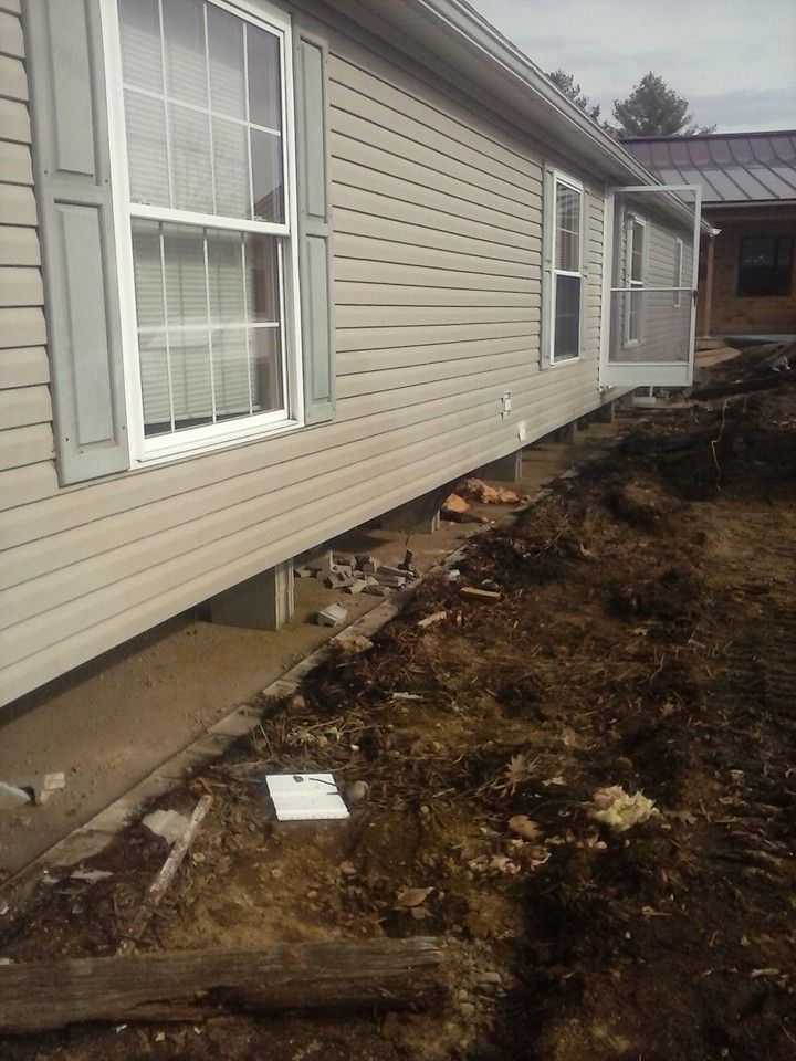 Side view of a house with concrete foundation. Dirt and construction materials surround the house.