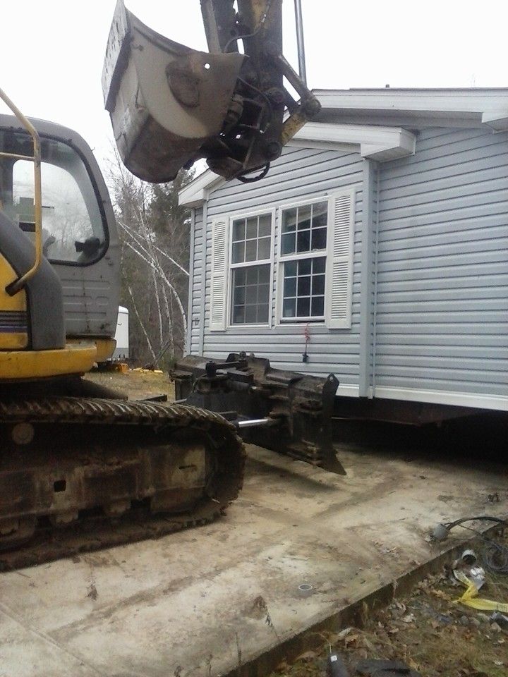 An excavator lifting a mobile home's bay window during a relocation or demolition process.