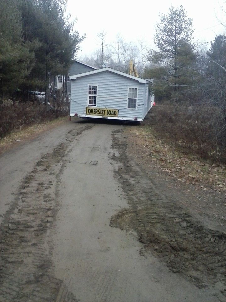 Mobile home being moved down a muddy dirt road, surrounded by trees.