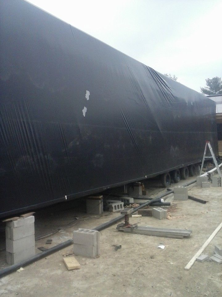 A large, black-covered structure elevated on cinder blocks, jacks, and beams; construction setting.