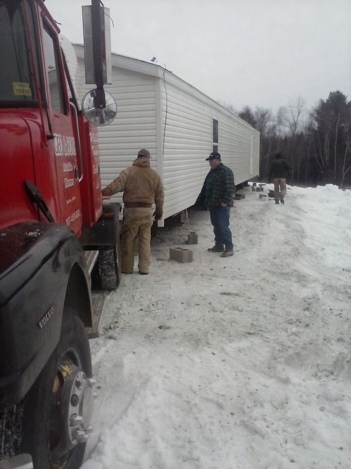 Two men working on a mobile home being moved by a red truck in a snowy area.