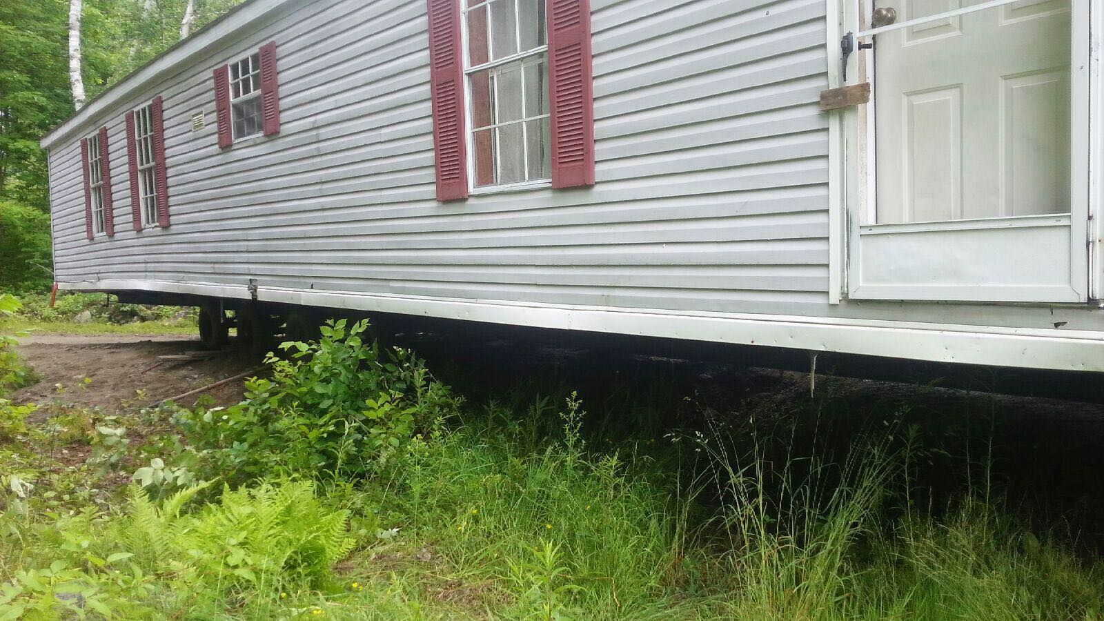 Mobile home with gray siding, red shutters, and white door, in overgrown grass.
