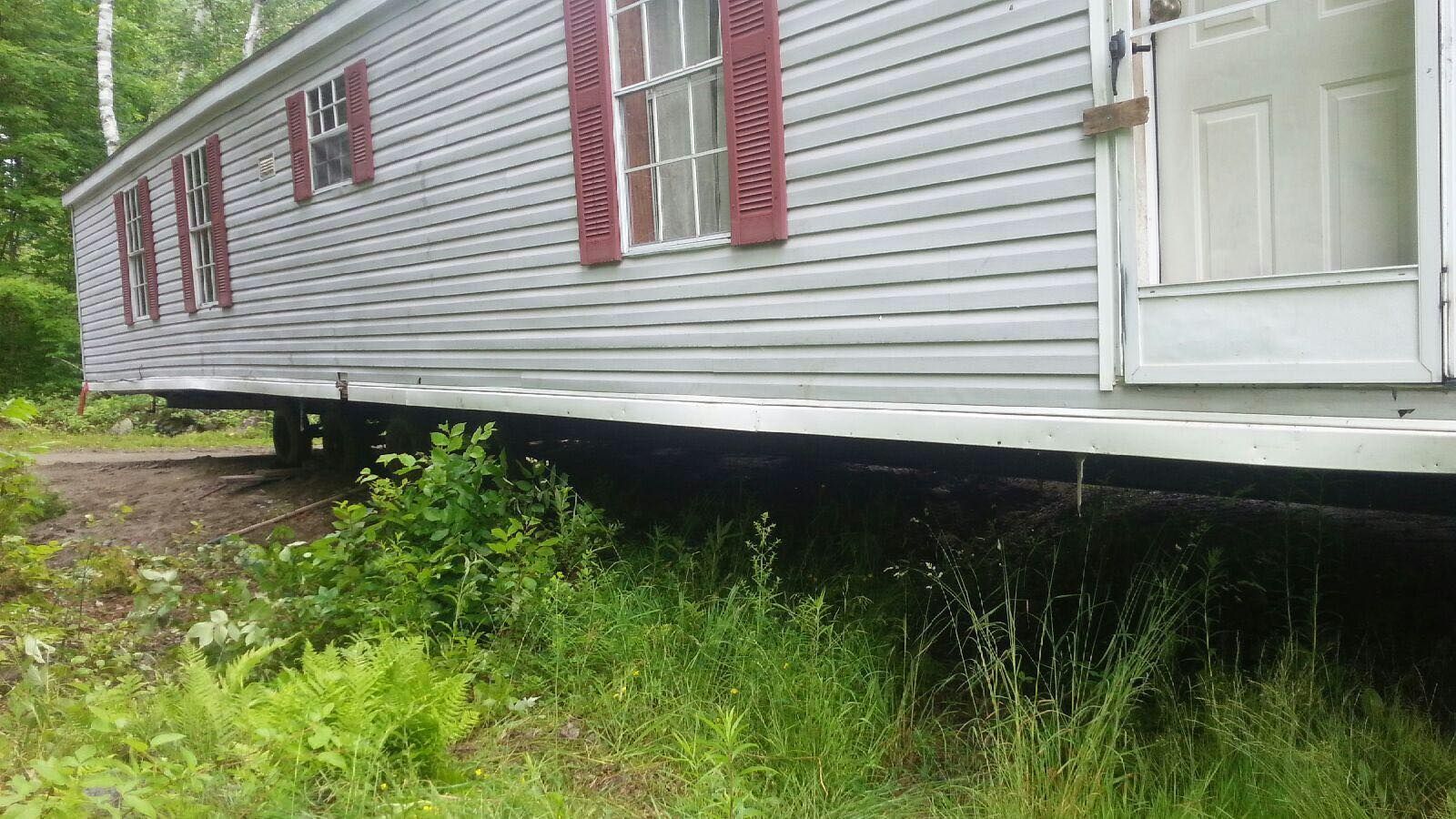 Gray mobile home with red shutters and door, set in tall grass.
